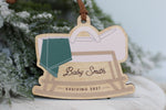 Personalized pregnancy announcement Christmas ornament featuring a wooden rocking baby cradle with a green blanket, custom Baby Smith name, and Arriving 2027, perfect for a holiday pregnancy reveal.