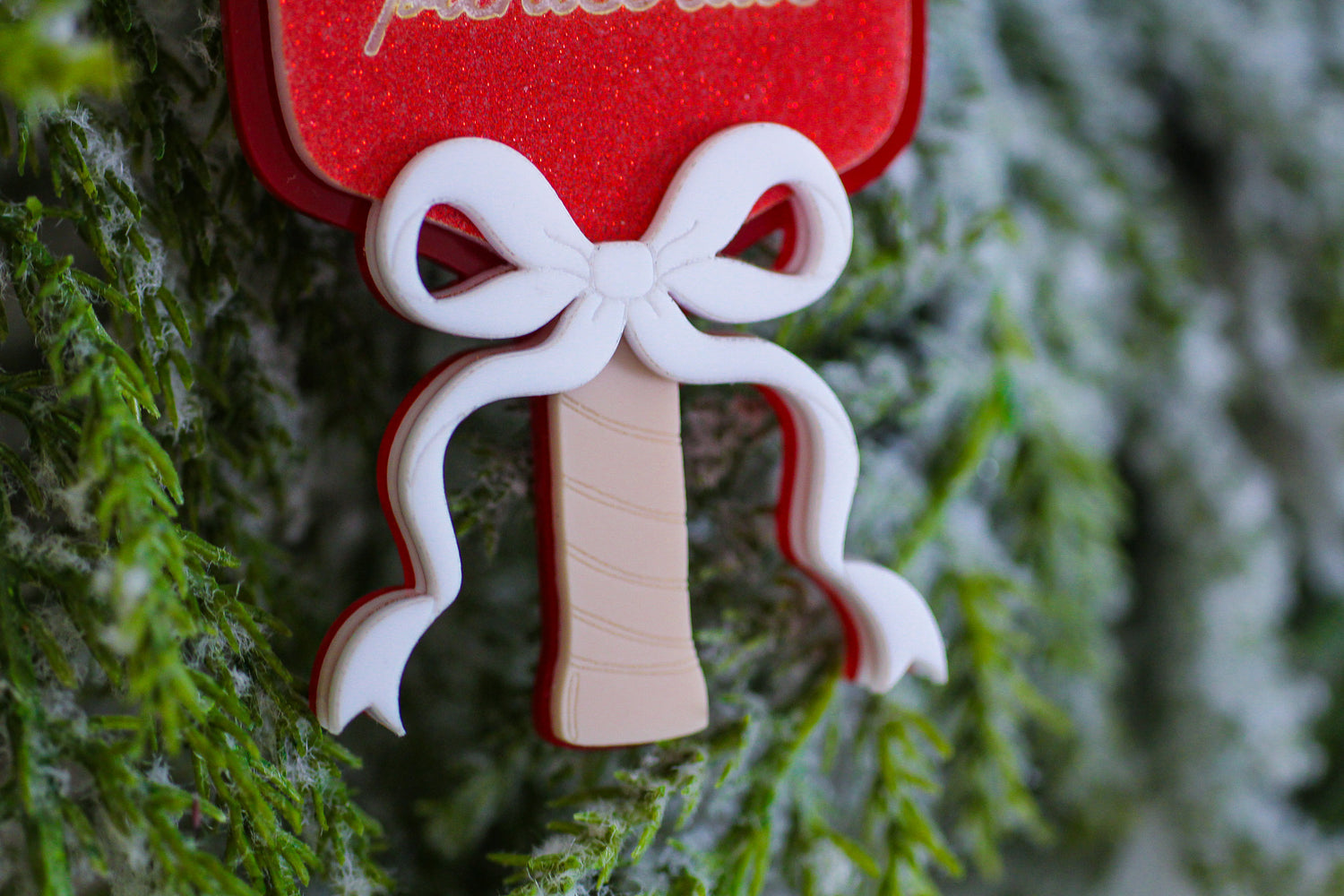 Close-up of a red glitter pickleball paddle Christmas ornament with a layered white bow and engraved wooden handle.