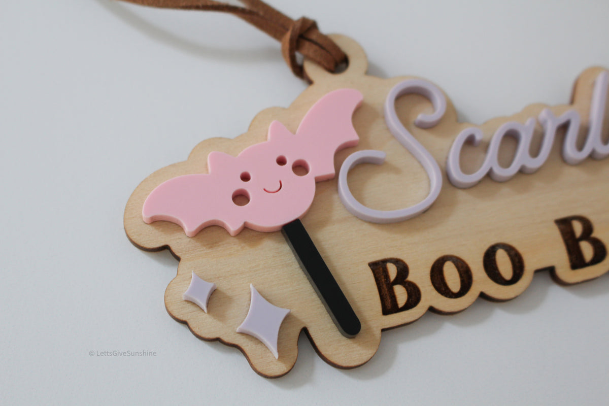Close-up of pink bat and personalized acrylic name on a wooden Boo Basket Halloween tag for kids