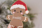 Custom name gingerbread man Christmas ornament made from layered wood and acrylic, featuring a red Santa hat, white icing details and Scarlett's name.