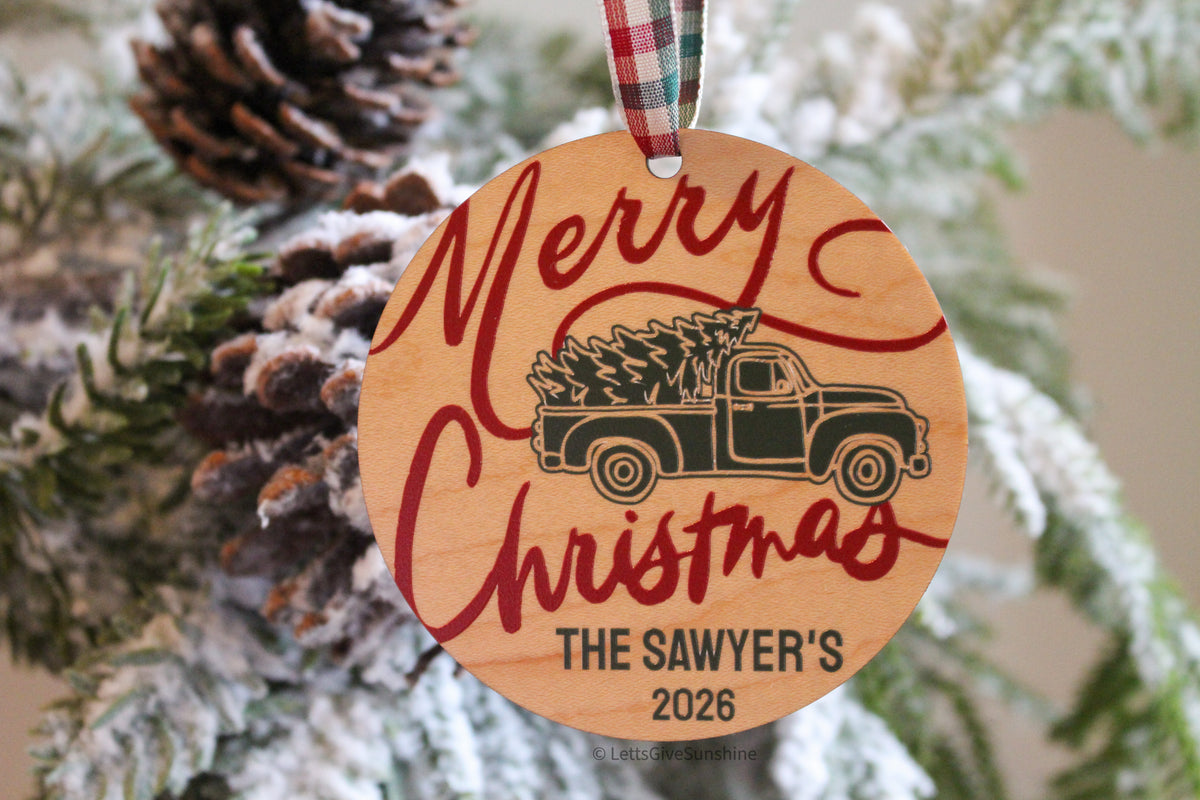 Custom family name Christmas ornament printed on natural finished wood with vintage Christmas tree truck design, personalized Sawyer family name and 2026 date.