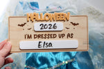 Reusable Halloween photo prop for kids with dry erase year and costume spaces, wooden board with orange Halloween lettering and bat details