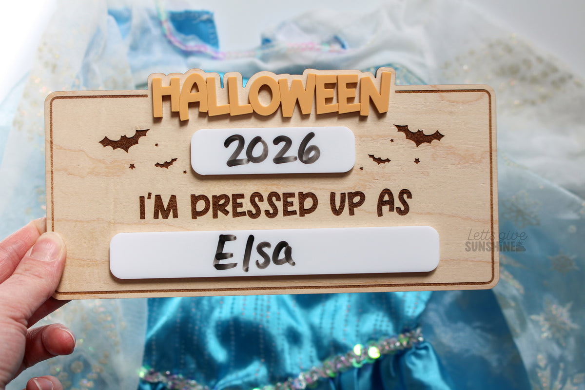 Reusable Halloween photo prop for kids with dry erase year and costume spaces, wooden board with orange Halloween lettering and bat details