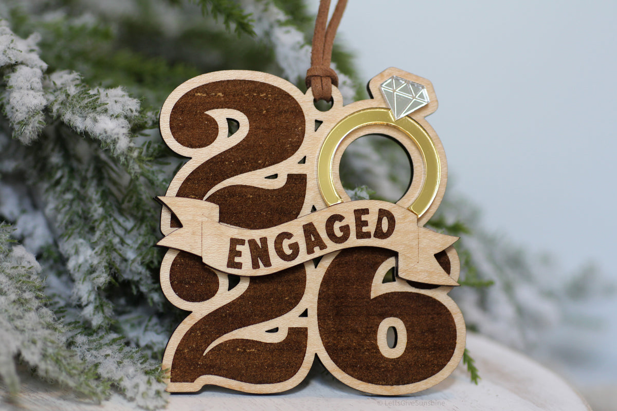 Engaged 2026 Christmas ornament made from wood with an engraved banner, gold acrylic engagement ring, and mirrored diamond, a keepsake for newly engaged couples.
