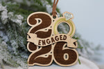 Engaged 2026 Christmas ornament made from wood with an engraved banner, gold acrylic engagement ring, and mirrored diamond, a keepsake for newly engaged couples.