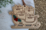 Custom family Christmas ornament 2026 featuring a wooden Santa sleigh filled with engraved name presents, layered holly berries, and a brown hanging ribbon.