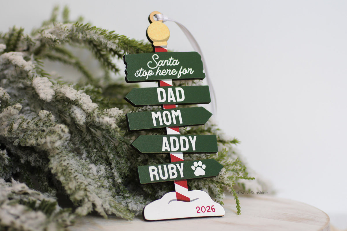 Personalized family Christmas ornament 2026 with green Santa Stop Here sign, custom family names, pet paw print, and wooden North Pole design