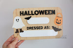 Reusable wooden Halloween photo prop board with dry erase spaces for the year and child’s costume, decorated with ghost, bats, and pumpkin bucket