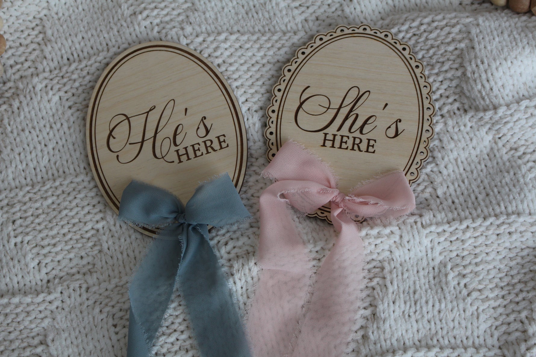 Wooden He’s Here and She’s Here baby announcement signs with blue and pink chiffon bows on a cozy knit blanket