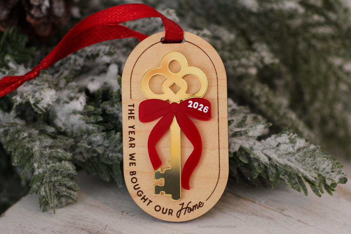 Wooden first Christmas in our new home ornament featuring a gold acrylic key, red bow with 2026 date, and engraved housewarming keepsake message.