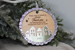 It Takes a Village 2026 Christmas ornament with engraved thank you message, silver glitter border and mirrored acrylic houses hanging on a snowy Christmas tree.