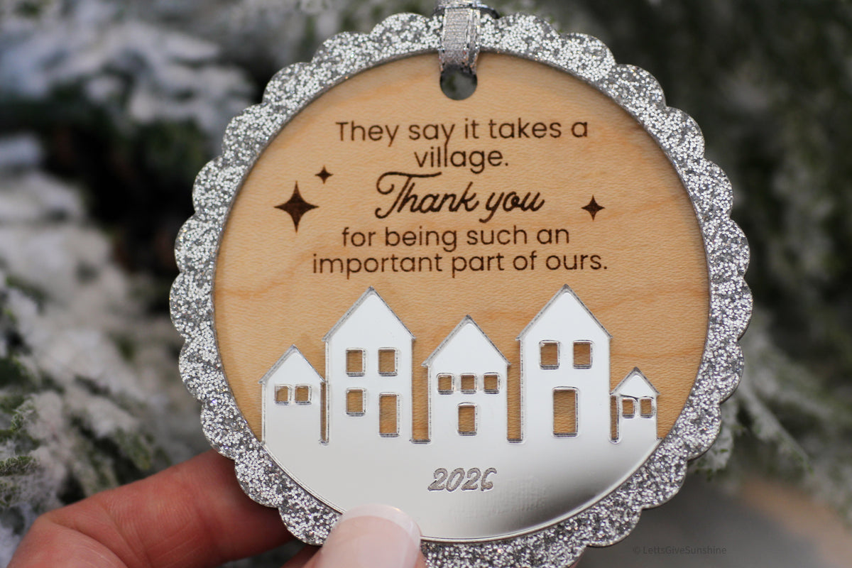 2026 It Takes a Village Christmas keepsake ornament with a scalloped silver glitter border, engraved appreciation message and layered silver acrylic village