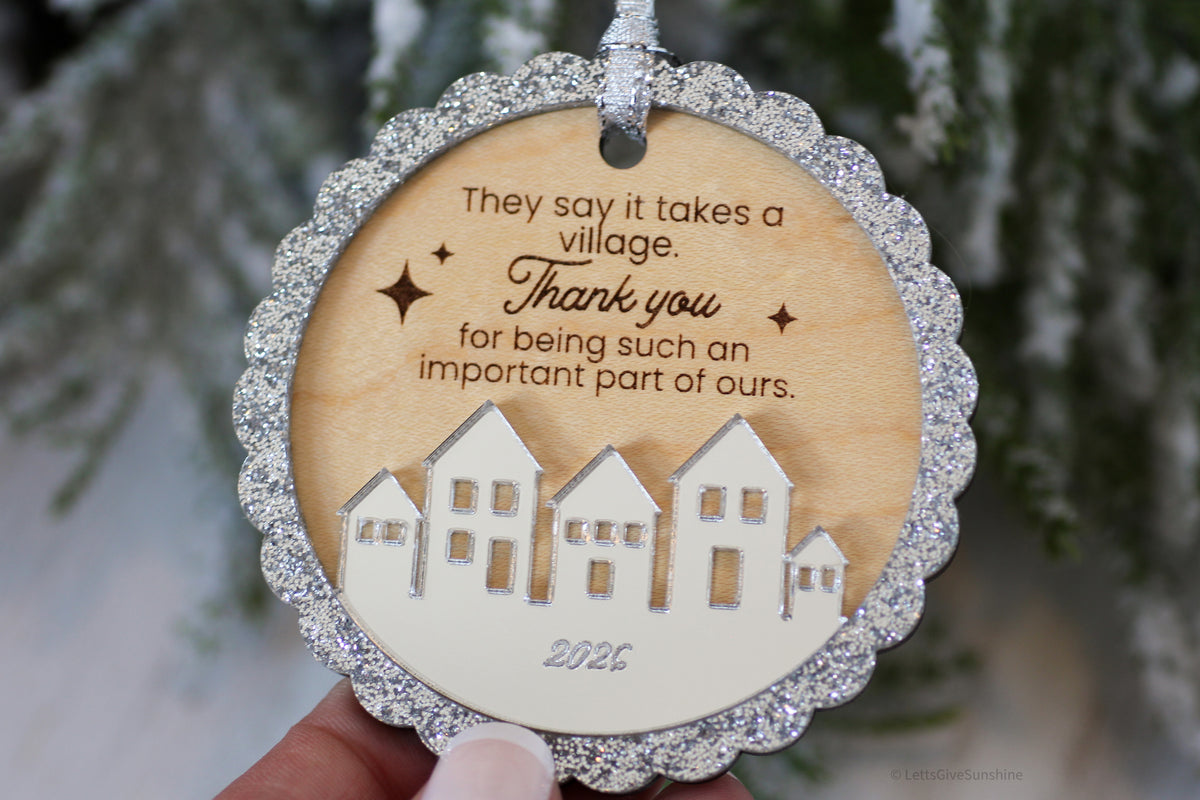 Daycare provider Christmas thank you gift featuring a wooden It Takes a Village ornament with engraved message, silver ribbon and decorative village design