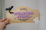 Personalized Halloween kids bookshelf sign featuring “Scarlett’s Spellbound Stories” and “batty about books,” with purple lettering, black bats and a white ghost on a wood background.