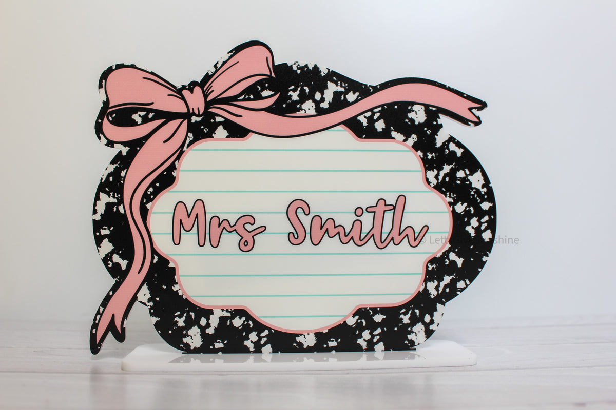 Personalized teacher name desk sign reading “Mrs Smith,” with pink bow, lined paper center and black-and-white pattern.