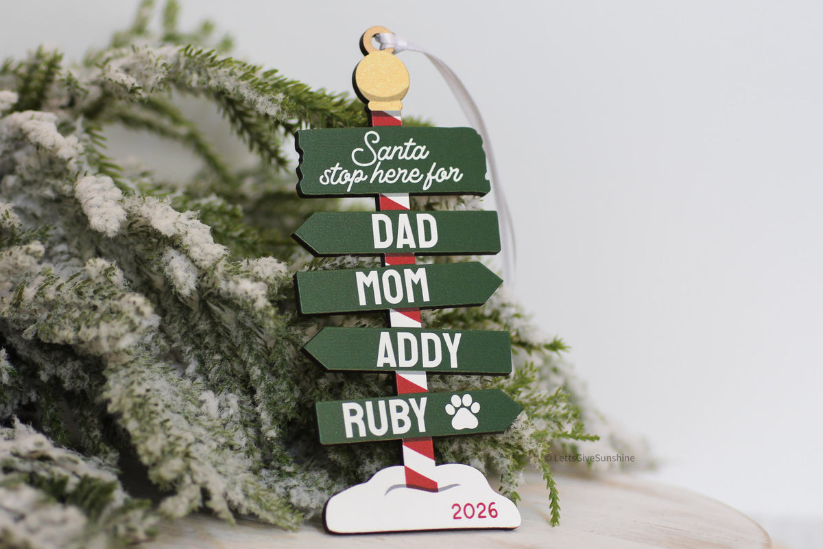 Personalized family Christmas ornament 2026 with green Santa Stop Here sign, custom family names, pet paw print, and wooden North Pole design