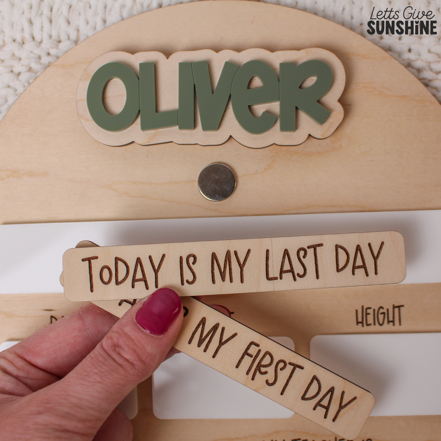 Close-up of a personalized first day of daycare board showing the name Oliver in raised green acrylic lettering and interchangeable wooden “Today Is My First Day” and “Today Is My Last Day” pieces.