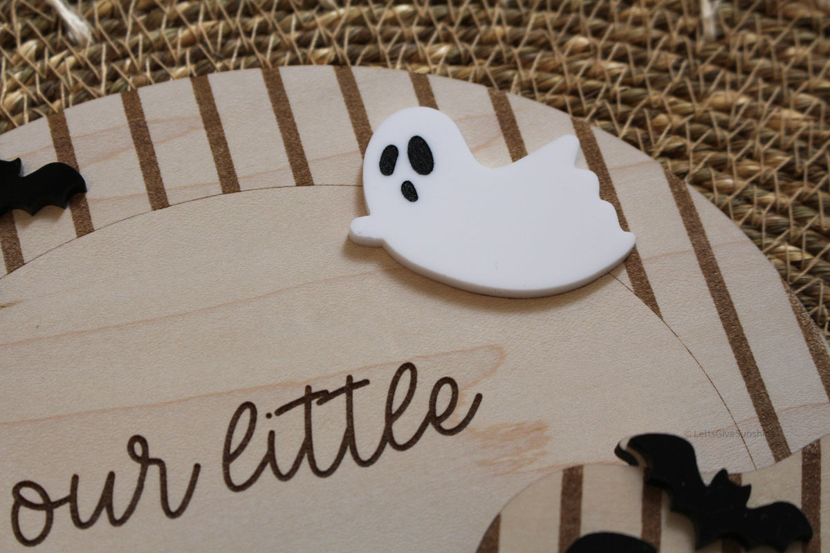 Close-up of personalized Our Little Boo Halloween footprint board featuring an engraved striped wood arch, white acrylic ghost, black bats and engraved lettering.