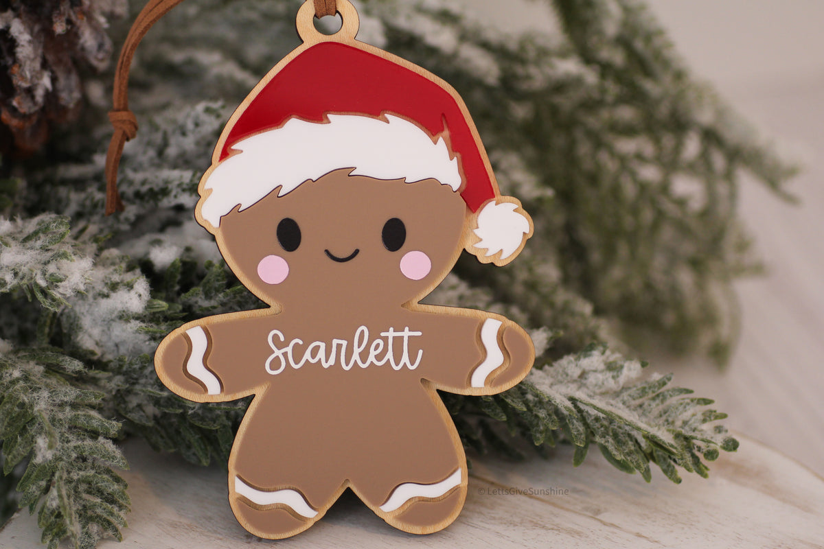 Personalized gingerbread Christmas ornament with Scarlett's name, red Santa hat, pink cheeks and layered acrylic details displayed on a snowy Christmas tree.