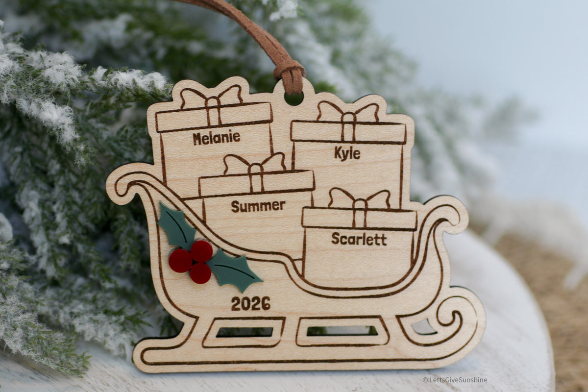 Personalized family Christmas ornament 2026 featuring a wooden Santa sleigh filled with engraved name presents, layered holly berries, and a brown hanging ribbon.