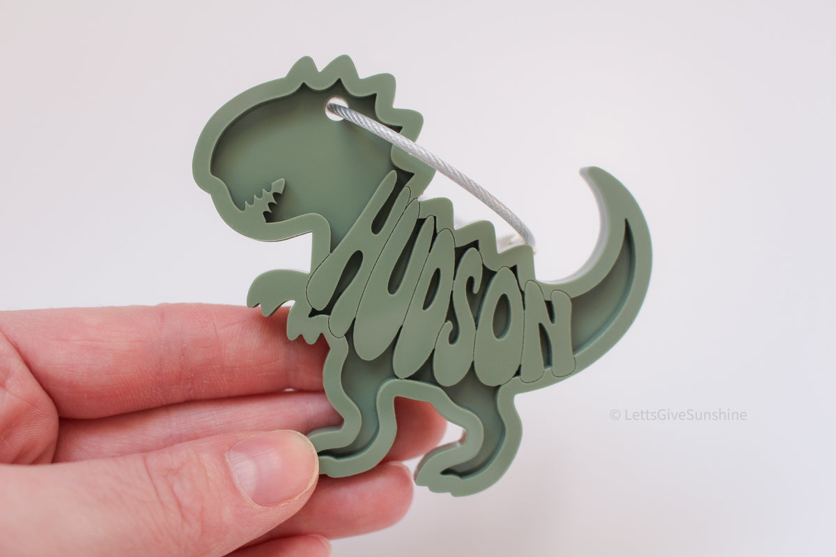 Personalized green dinosaur bag tag with the name Tyson cut into the acrylic design and a silver cable loop.