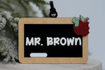 Personalized teacher Christmas ornament featuring a mini classroom chalkboard with Mr. Brown in white lettering, wooden frame, red apple and cute green worm.