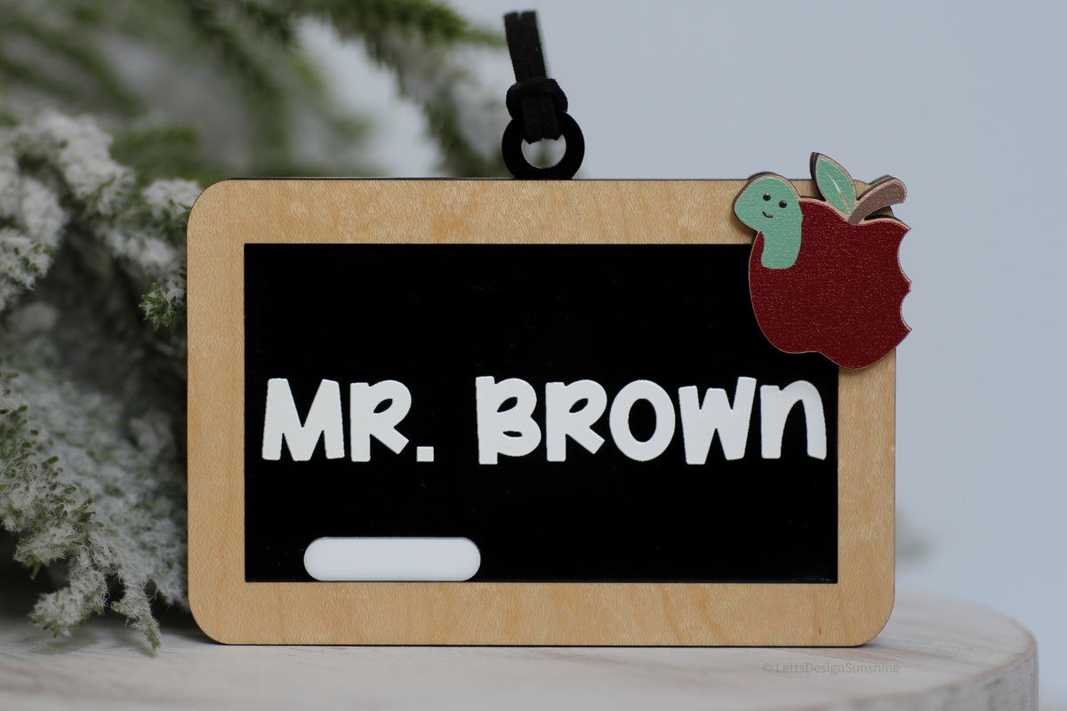 Personalized teacher Christmas ornament featuring a mini classroom chalkboard with Mr. Brown in white lettering, wooden frame, red apple and cute green worm.