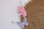 Personalized pink unicorn and lavender butterfly acrylic bag tags with the names Summer and Scarlett, attached to a woven backpack.