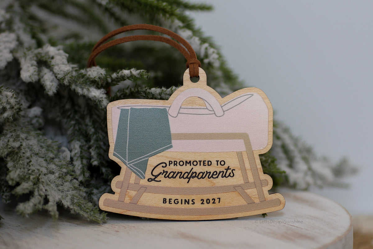 Grandparents pregnancy announcement Christmas ornament made from natural wood, featuring a rocking cradle, baby blanket and the words Promoted to Grandparents Begins 2027.