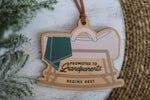 Wooden baby announcement ornament with Promoted to Grandparents Begins 2027 message, rocking bassinet design and brown faux suede hanging cord.