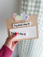 Personalized first day of school photo prop board with rainbow name detail, maple wood backing, dry erase acrylic area, and interchangeable “My first day of” and “My last day of” pieces.