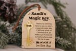 Santa's Magic Key wooden Christmas Eve keepsake with gold acrylic key, engraved no chimney message and brown hanging cord displayed on a snowy Christmas tree.