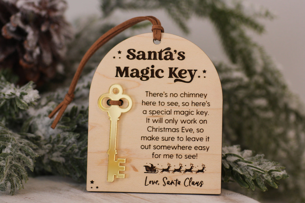 Santa's Magic Key wooden Christmas Eve keepsake with gold acrylic key, engraved no chimney message and brown hanging cord displayed on a snowy Christmas tree.