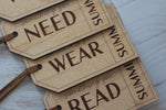 Close-up of engraved wooden Christmas gift tags for the four-gift tradition, featuring Need, Wear and Read labels with personalized name.