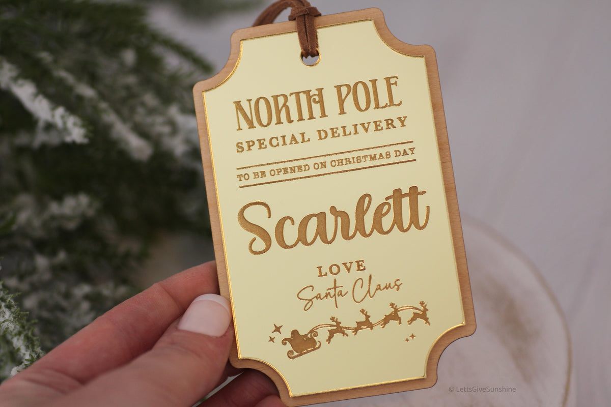 Personalized Santa Christmas present tag with reflective gold acrylic, engraved Scarlett name, North Pole Special Delivery wording and reindeer details.