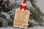 Wooden teacher Christmas ornament shaped like a cutting board with Recipe for the Perfect Teacher engraving, red bow, and 2026 rolling pin detail.