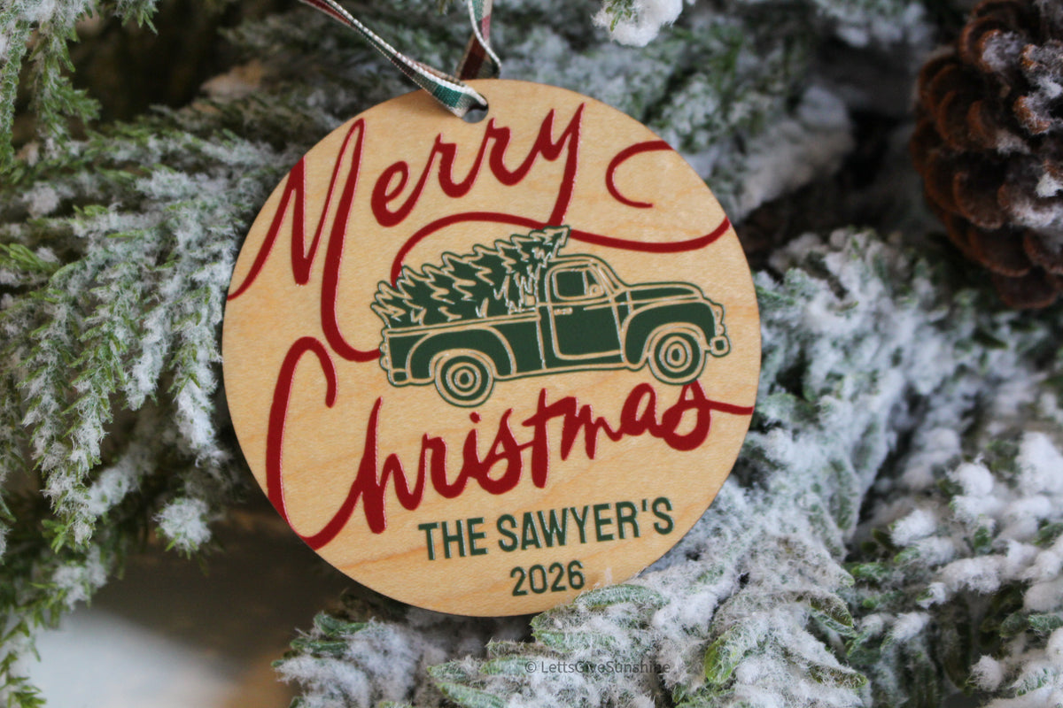 Personalized wooden family Christmas ornament featuring a green vintage pickup truck carrying a Christmas tree, red Merry Christmas lettering and The Sawyer's 2026.